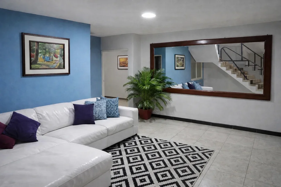 Sala interior con sof&aacute; blanco, pared azul y espejo amplio